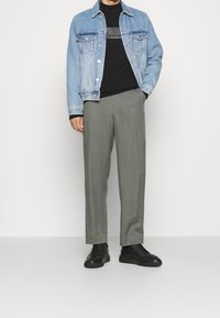 Ljusblå denimjacka, svart t-shirt med logotyp, grå tapered byxor och svarta sneakers. Avslappnad outfit med lager på lager-element.