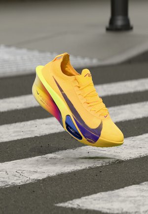 Zapatilla de running amarilla brillante con acentos morados, textura de punto y una suela multicolor. Presenta la marca Nike Air Zoom y un diseño elegante.