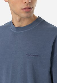 Mėlynas medvilnės marškinėliai su apvalia iškirpte, trumpomis rankovėmis ir reljefiniu "PEGADOR" logotipu kairėje krūtinės pusėje. Minkšta tekstūra, laisvas siluetas.