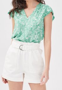 Blouse à imprimé floral vert avec un décolleté en V et des manches courtes, associée à un short taille haute blanc avec passants de ceinture et poches.