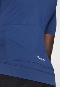 Jersey de ciclismo azul marino hecho de una tela suave y ligera con mangas cortas y un bolsillo trasero; presenta el logo blanco de "Rapha".