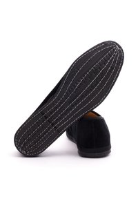 Schwarzer Slip-on-Schuh aus Wildleder mit einer strukturierten schwarzen Gummisohle und weißen Nähten, der eine runde Zehenpartie und ein minimalistisches Design aufweist.