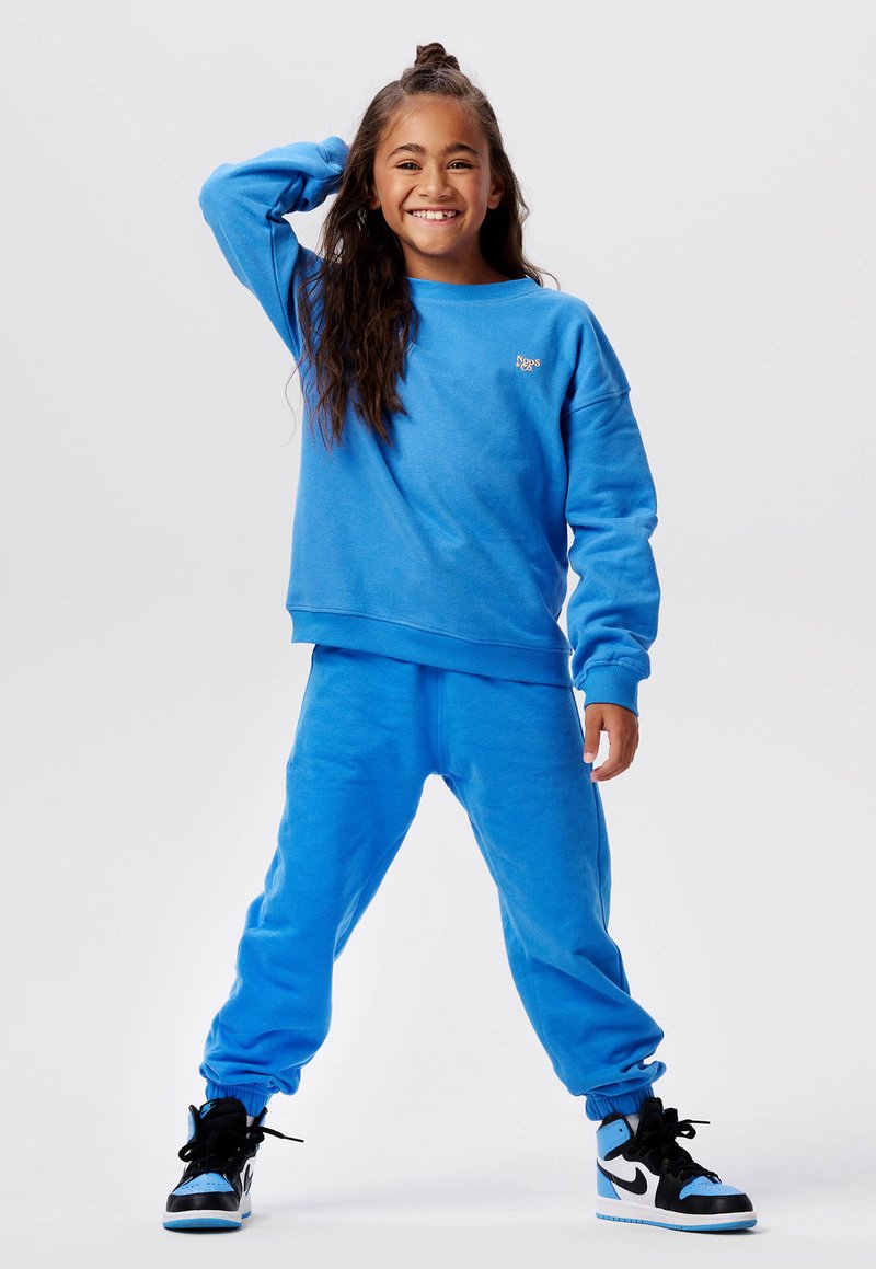 Blauwe sweatshirt en bijpassende sweatpants set, gemaakt van zachte katoen, met ribgebreide manchetten en een klein logo detail. Zwarte en blauwe hoge sneakers.