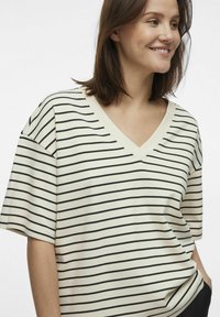 Stribet T-shirt i krem og sort, V-hals design, afslappet pasform, korte ærmer, blødt bomuldsmateriale, med vandrette striber.