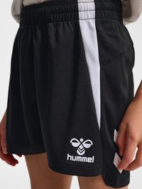 Gros plan d'une personne portant un short de sport noir avec une bande verticale blanche et le logo Hummel sur la jambe gauche.