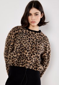 Pull en imprimé léopard beige et noir, fabriqué dans un matériau doux et texturé, avec un col rond noir et une coupe décontractée.