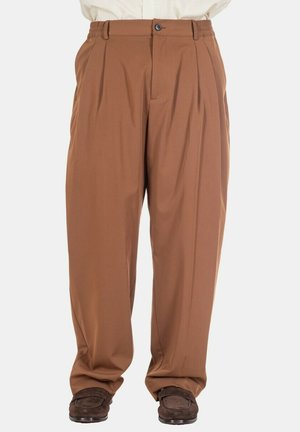 Braune plissierte Hosen mit Knopf und Reißverschluss, getragen mit dunkelbraunen Loafern, von der Taille bis zu den Füßen vor einfarbigem Hintergrund gezeigt.