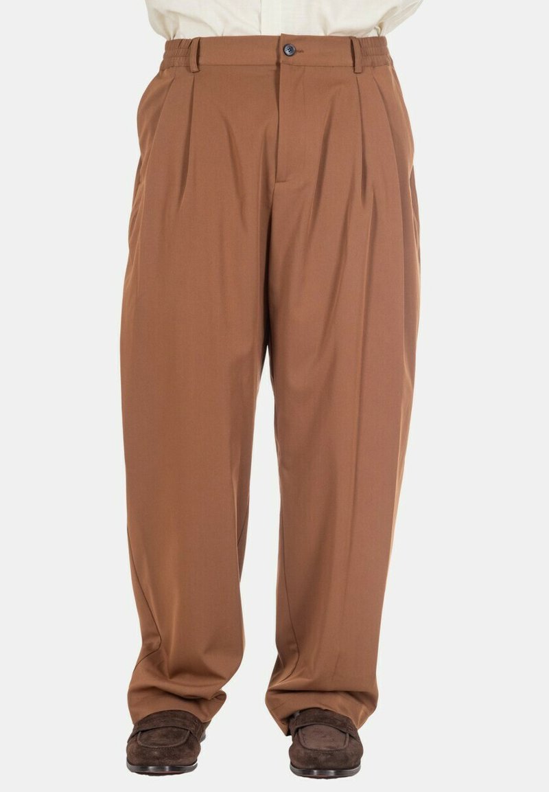 Pantalon marron plissé avec bouton et fermeture éclair, porté avec des mocassins marron foncé, présenté de la taille jusqu'aux pieds sur un fond uni.