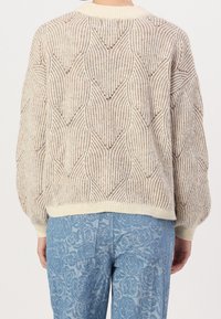 Gestrickter Pullover in Creme mit einem strukturierten Diamantmuster, ausgestattet mit einem gerippten Rundhalsausschnitt und ballonförmigen Ärmeln, kombiniert mit hellblauen gemusterten Hosen.
