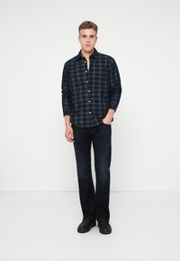 Marine rute flanellskjorte med knappelukking, lange ermer og en avslappet passform, parret med mørke denimjeans og svarte sko.