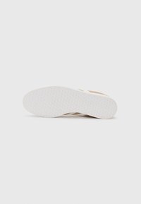 Semelle de sneaker beige avec un fond en caoutchouc blanc texturé, présentant un motif en nid d'abeille et une couleur beige discrète sur le côté.