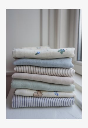 Zložena skladovnica sedmih kosov mehke tkanine v svetlih barvah in vzorcih, postavljena blizu okna na beli površini.