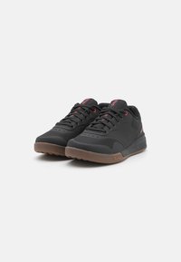 Black athletic shoes with red accents, smooth synthetic upper, textured rubber sole, and classic lace-up design.