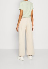 Light green short-sleeve t-shirt paired with cream wide-leg trousers. Trousers feature an elastic waistband and soft, textured fabric.