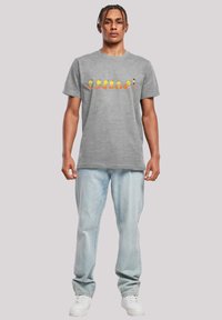 Grå bomull T-skjorte med tegneserie grafikk av gule fugler i ulike posisjoner. Kombinert med lyseblå denimjeans og hvite joggesko.