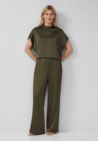 Combinaison olive verte avec manches courtes, col montant, taille élastique et pantalon large. Tissu lisse avec une texture douce. Design minimaliste.