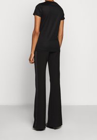Camiseta negra ajustada con mangas enrolladas, combinada con pantalones negros de campana que presentan dos rayas verticales a lo largo de los lados. Textura mate.