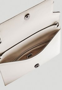 Biała skórzana kopertówka otwarta, pokazująca wewnętrzną kieszeń na zamek i zapięcie na zatrzask na jednolitym jasnoszarym tle.