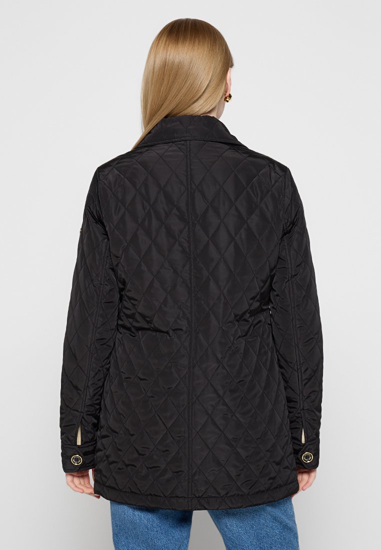 Veste matelassée noire avec un col montant, présentant un motif en losanges et des accents de boutons sur les manches. Texture lisse, design mi-long.