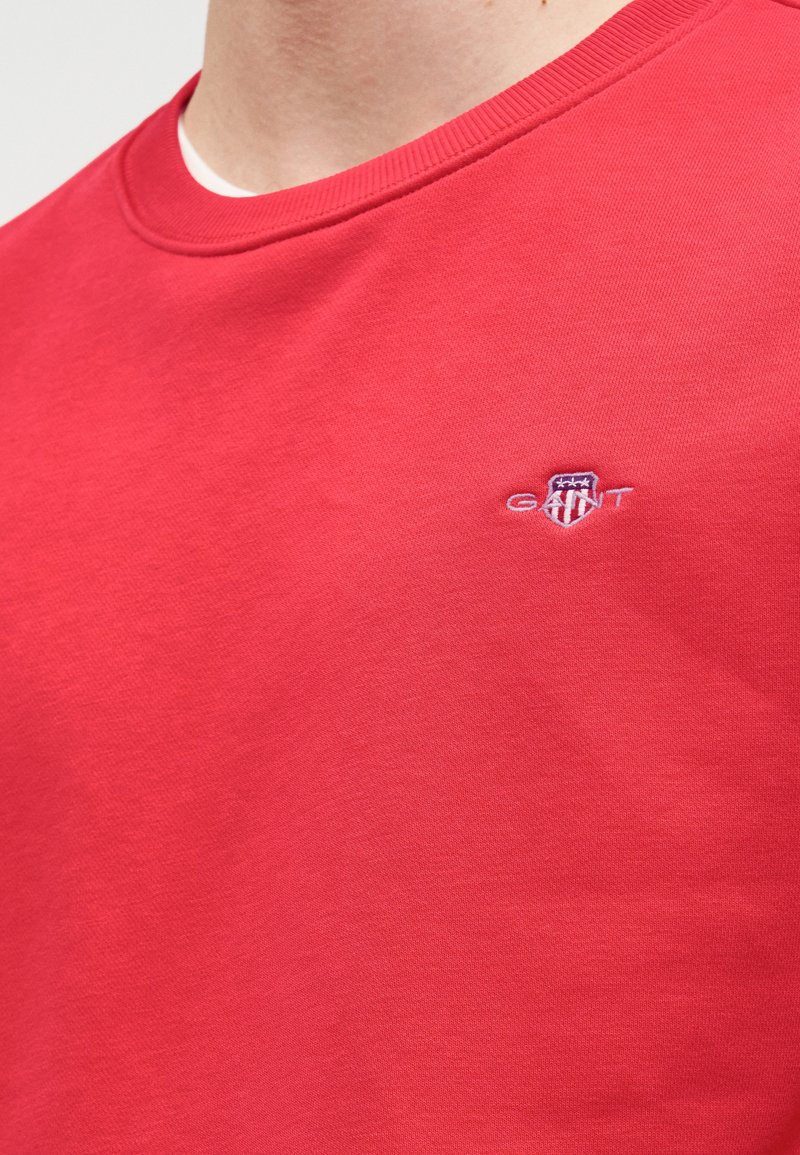 Felpa in cotone rossa con collo tondo e polsini a coste. Presenta un piccolo logo ricamato sul petto. Tessuto morbido, design casual.