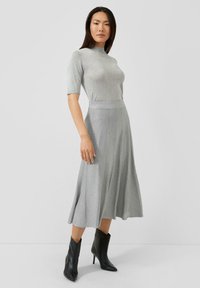 Szary, dopasowany top z krótkim rękawem połączony z lejącą się, sięgającą kostek szarą spódnicą. Całość uzupełniają czarne botki za kostkę. Gładka tekstura w całym stroju.