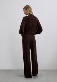 Conjunto marrón de dos piezas tejido, con diseño texturizado, mangas largas y pantalones de pierna ancha, con un ajuste relajado y bordes acanalados.