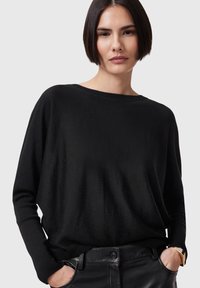 Black, long-sleeve sweater in a soft, smooth fabric with a loose fit and wide neckline, paired with sleek black leather pants.