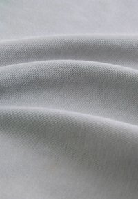 Tela gris claro con una textura suave, mostrando suaves pliegues. El material parece ligero con un sutil patrón de tejido.