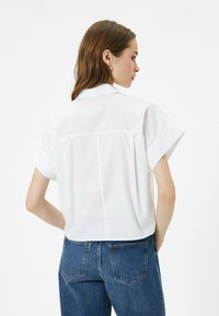 Camicetta bianca a maniche corte con colletto classico, linee pulite e design dritto sul retro. Abbinata a jeans in denim blu a vita alta.