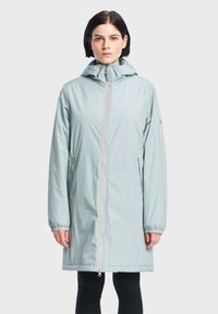 Cappotto lungo impermeabile azzurro chiaro con cappuccio, cerniera frontale, polsini elasticizzati e tasche laterali. Finitura liscia con dettagli di cucitura sottili.