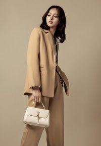 Completo beige con pantaloni a gamba larga e blazer strutturato. Borsa bianca con hardware dorato, manico piccolo e dettaglio a chiusura.