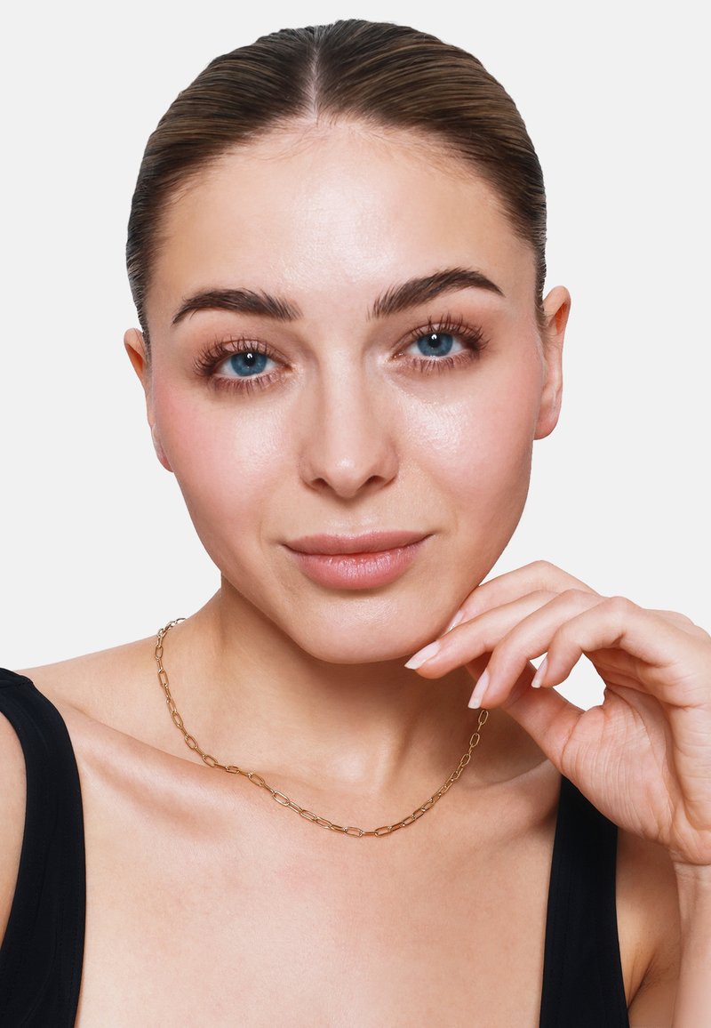 Goldene Halskette mit elongated Gliedern, um den Hals getragen. Das Model hat helle Haut, kurze Haare und blaue Augen und präsentiert die Details der Kette.