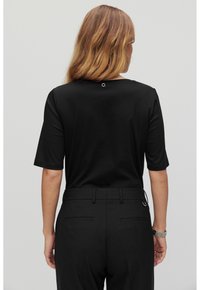 Musta lyhythihainen paita pyöreällä kaula-aukolla, jossa on hienovarainen koristeellinen silmukka takana. Yhdistetty korkea vyötärö mustiin housuihin.