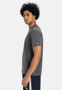 Grijs T-shirt met korte mouwen en een ronde halslijn, met een logo op de linkermouw. Draagt bij donkere shorts in een zijaanzicht.