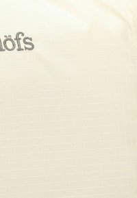 Tissu beige clair avec un motif à carreaux. Présente un texte brodé en gris. Texture lisse, design léger adapté à une utilisation en extérieur.