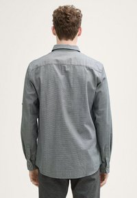 Chemise à manches longues à carreaux gris avec un col boutonné, présentant un ourlet droit et des poignets boutonnés, fabriquée en tissu texturé.