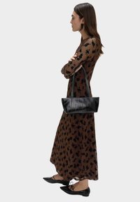 Černá texturovaná kabelka s dvěma uchy, obdélníkového tvaru, nošená s hnědými šaty s květinovým vzorem a černými plochými botami.