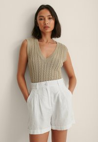 Beige strikket tanktop med V-hals og tekstureret design, parret med hvidt linned shorts med folder og knaplukning.