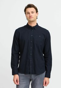 Mørk marinblå skjorte med lange ermer, brystlomme og en jevn tekstur. Kombinert med lys grå denim.