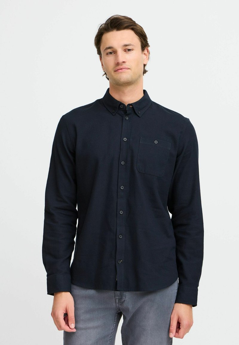 Mørk marinblå skjorte med lange ermer, brystlomme og en jevn tekstur. Kombinert med lys grå denim.