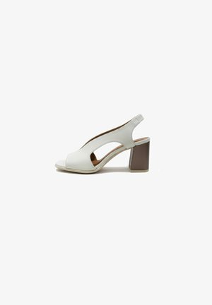 Witte open teen slingback sandaal met uitgesneden zijkanten en een stevige bruine blokhak op een witte achtergrond.