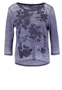 Violetti pitkähihainen paita, jossa on kukkakuosi ja painettu teksti. Pehmeä kangas, pyöreä pääntie ja kaareva helma, joissa on rento istuvuus.
