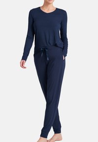 Marinblå långärmad topp med V-ringning och matchande byxor som har dragsko i midjan och sidofickor; mjukt tyg och figurnära design.