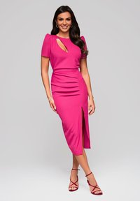 Robe fuchsia au design cintré, avec des manches bouffantes, une découpe latérale et une fente sur le côté ; tissu lisse et légère fronce à la taille. Talons à brides.