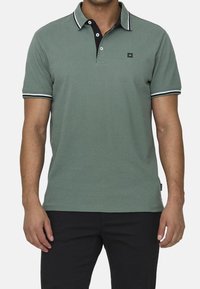 Groen poloshirt met korte mouwen, zwarte kraag en witte details. Bevat een drieknoopsluiting en een klein logo op de borst.