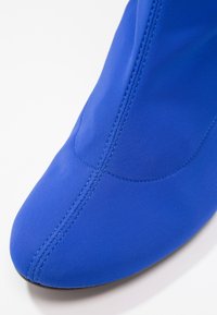 Chaussure en tissu bleu vif avec coutures apparentes le long de l'avant arrondi et de la partie supérieure sur fond blanc.