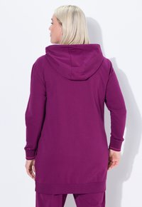 Haut à capuche long violet avec capuche, manches longues et poignets côtelés. Tissu lisse avec une coupe décontractée, descendant en dessous des hanches.