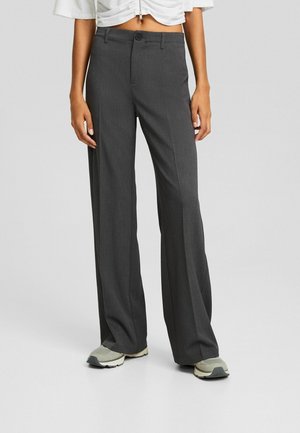 Person wearing high-waisted, wide-leg dark gray trousers paired with light gray athletic shoes on a plain background.