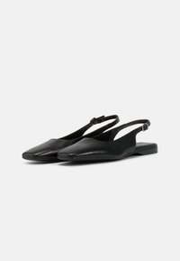 Chaussures slingback en cuir noir avec un nez pointu, un talon plat et un design minimaliste. Elles disposent d'une sangle au niveau de la cheville ajustable pour un maintien sécurisé.