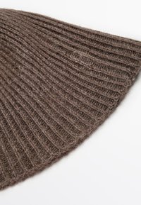 Cappello a coste marrone realizzato in materiale morbido, con un orlo curvo e una superficie testurizzata per calore e comfort.